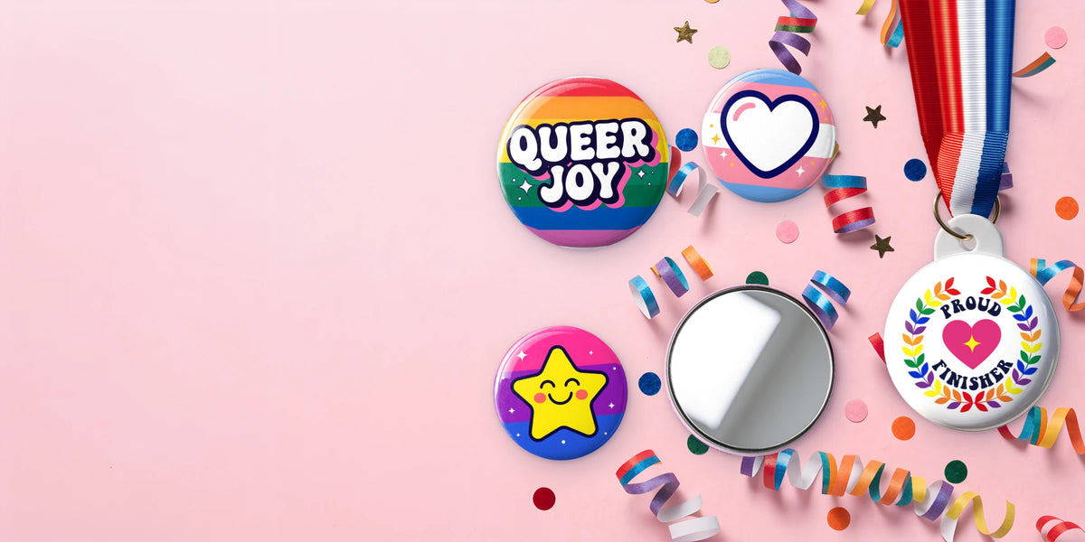 Custom pride pin badges, a pocket mirror and a Proud Finisher medal on pink with rainbow streamers