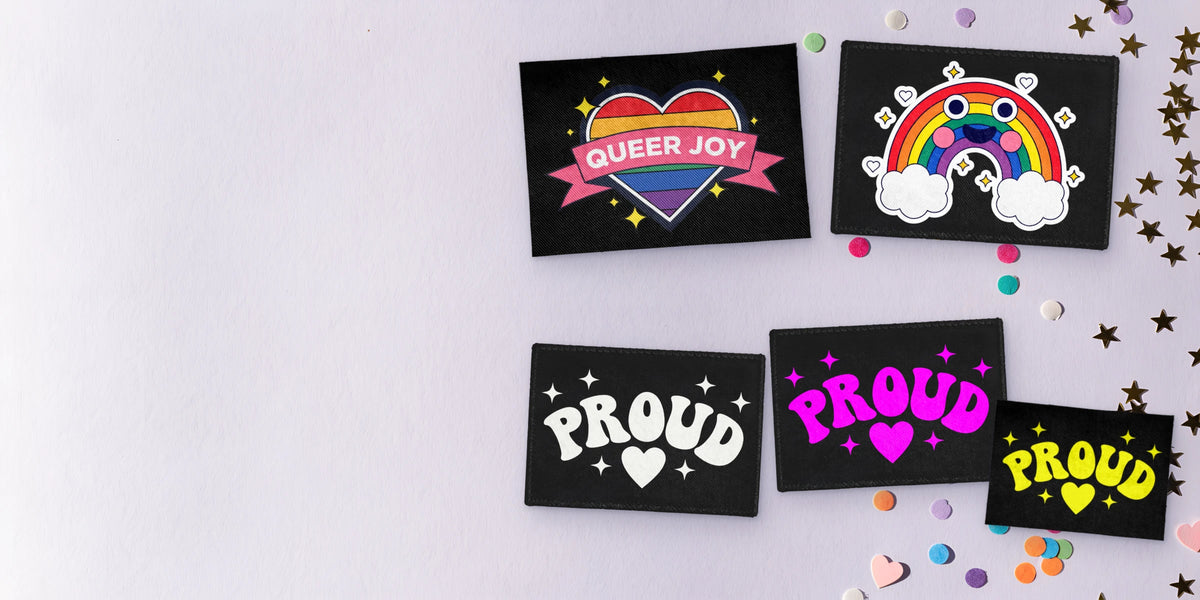 Custom sew-on patches laid flat: a Queer Joy rainbow heart, a smiling rainbow and Proud patches