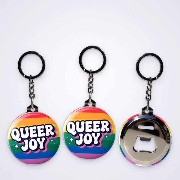 Custom bottle opener keyrings printed with Queer Joy on rainbow stripes, shown with the bottle opener back