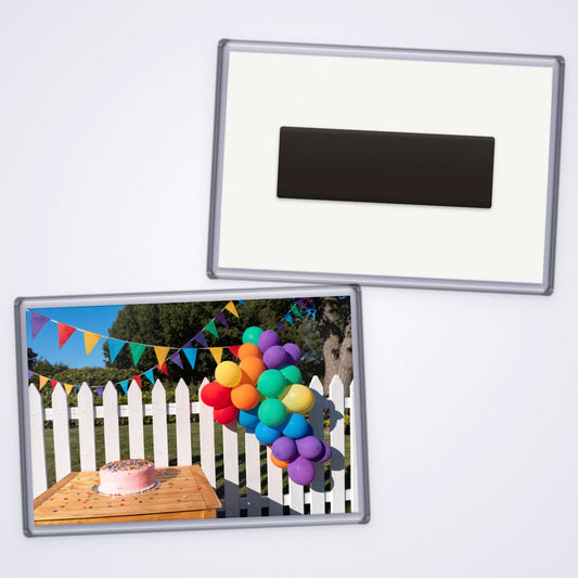 Custom 90x60mm jumbo photo magnet showing rainbow balloons and bunting at a garden party, with the magnet back