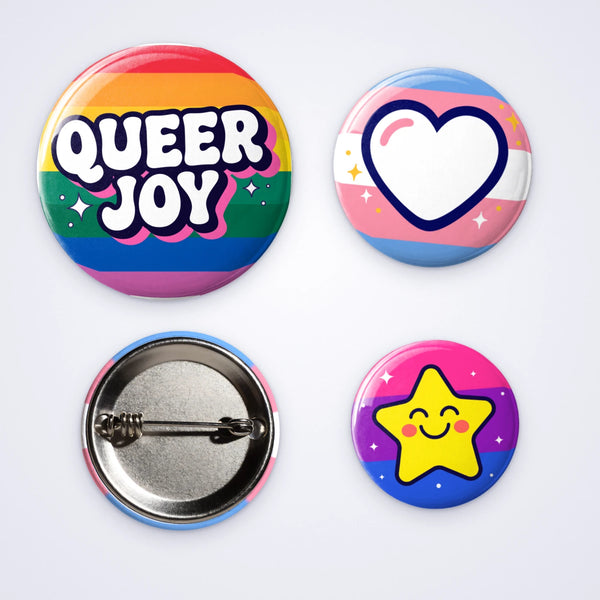 Custom pin badges in three sizes: Queer Joy on rainbow stripes, a heart on trans pride stripes and a smiling star on bi pride stripes, with a pin back